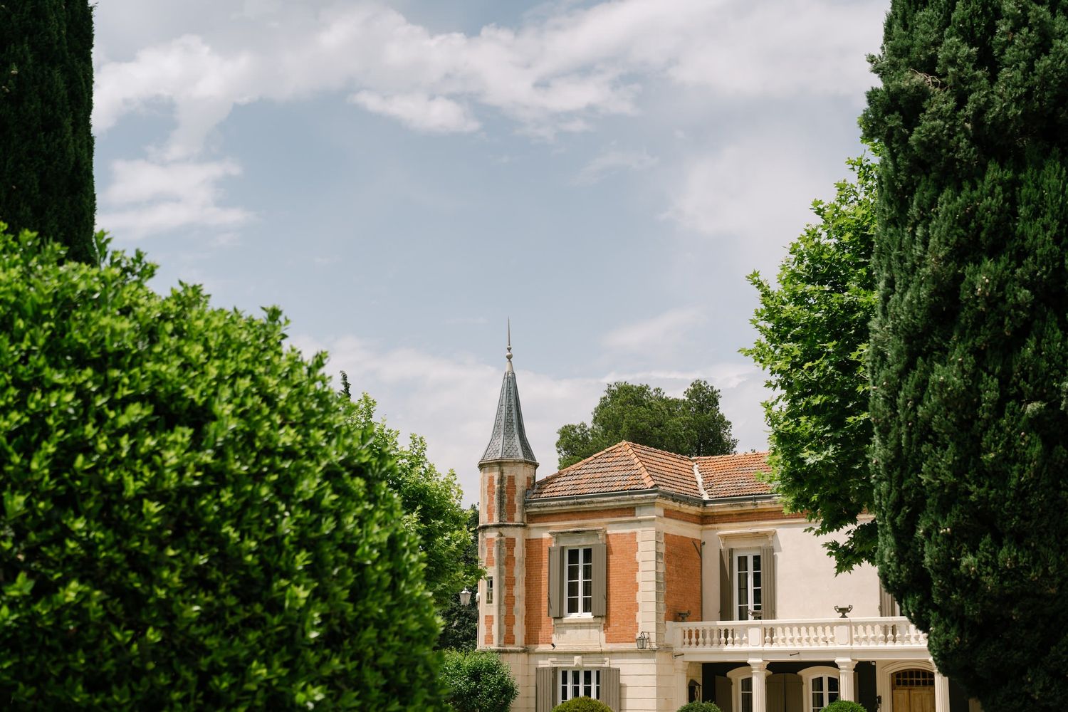 Elegant French-style mansion with a spired tower visible through green trees.