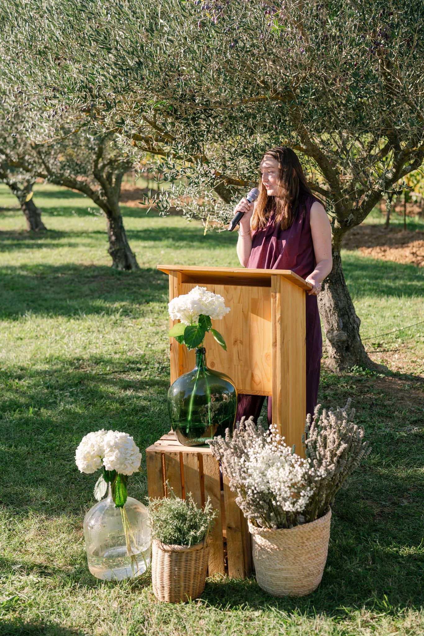 Rustic wooden podium decorated with white hydrangeas and flowers stands in an olive grove.