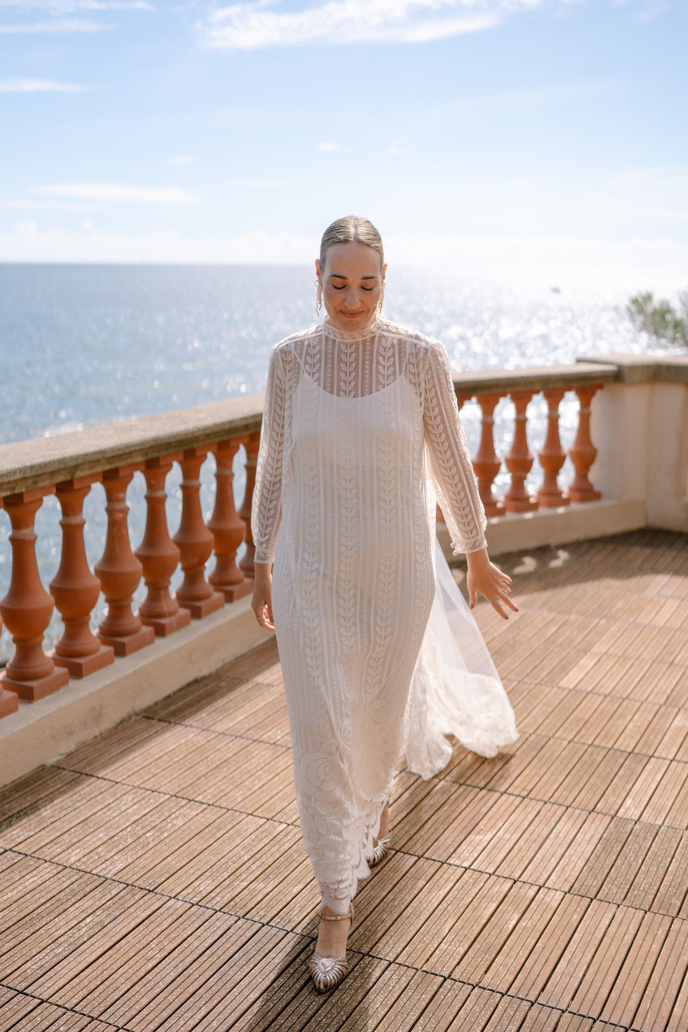 Sunlit terrace with ornate stone railings showcasing a flowing white wedding dress.