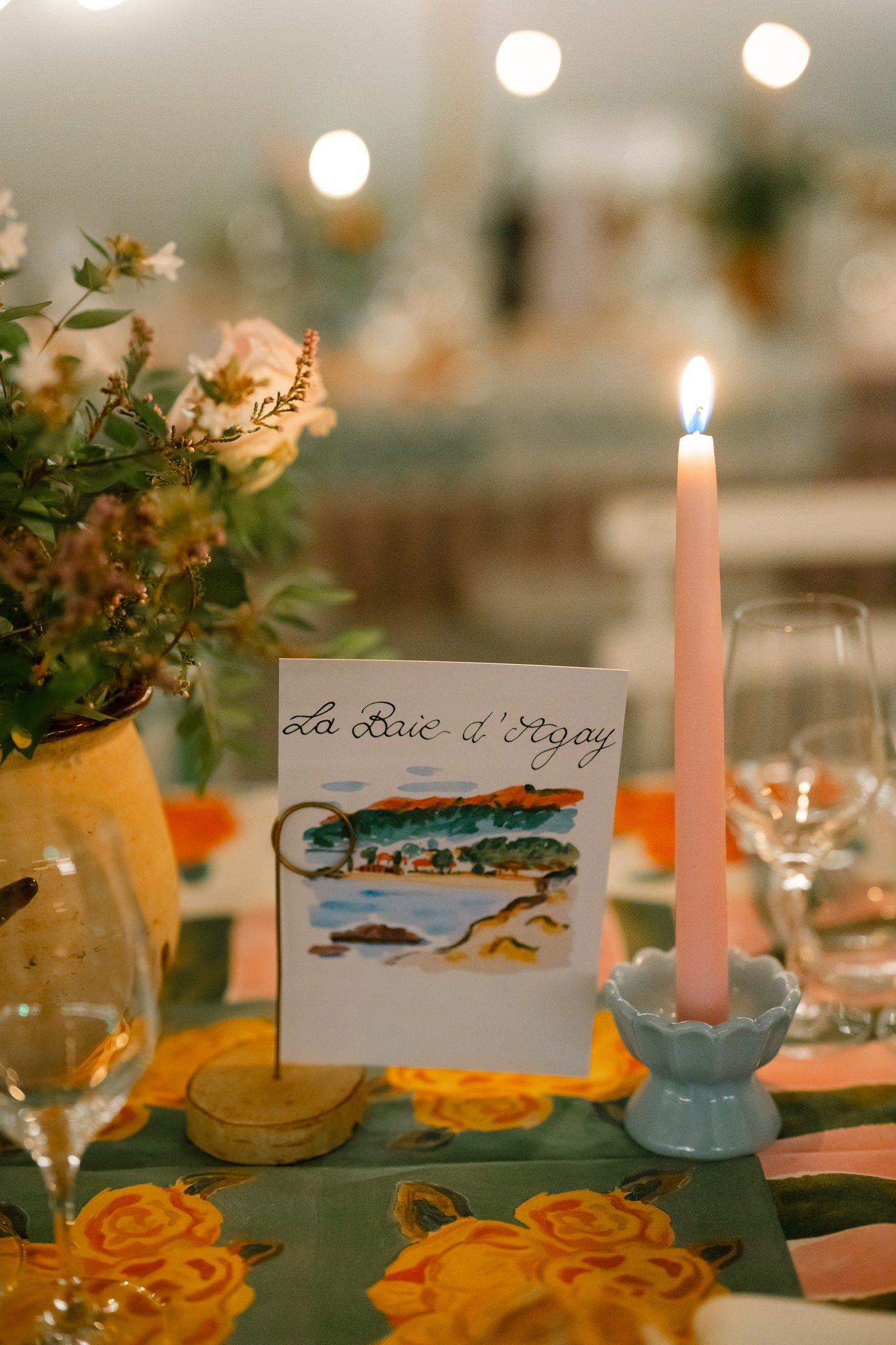 Wedding reception table decorated with candles and handpainted place cards showing coastal scenes.