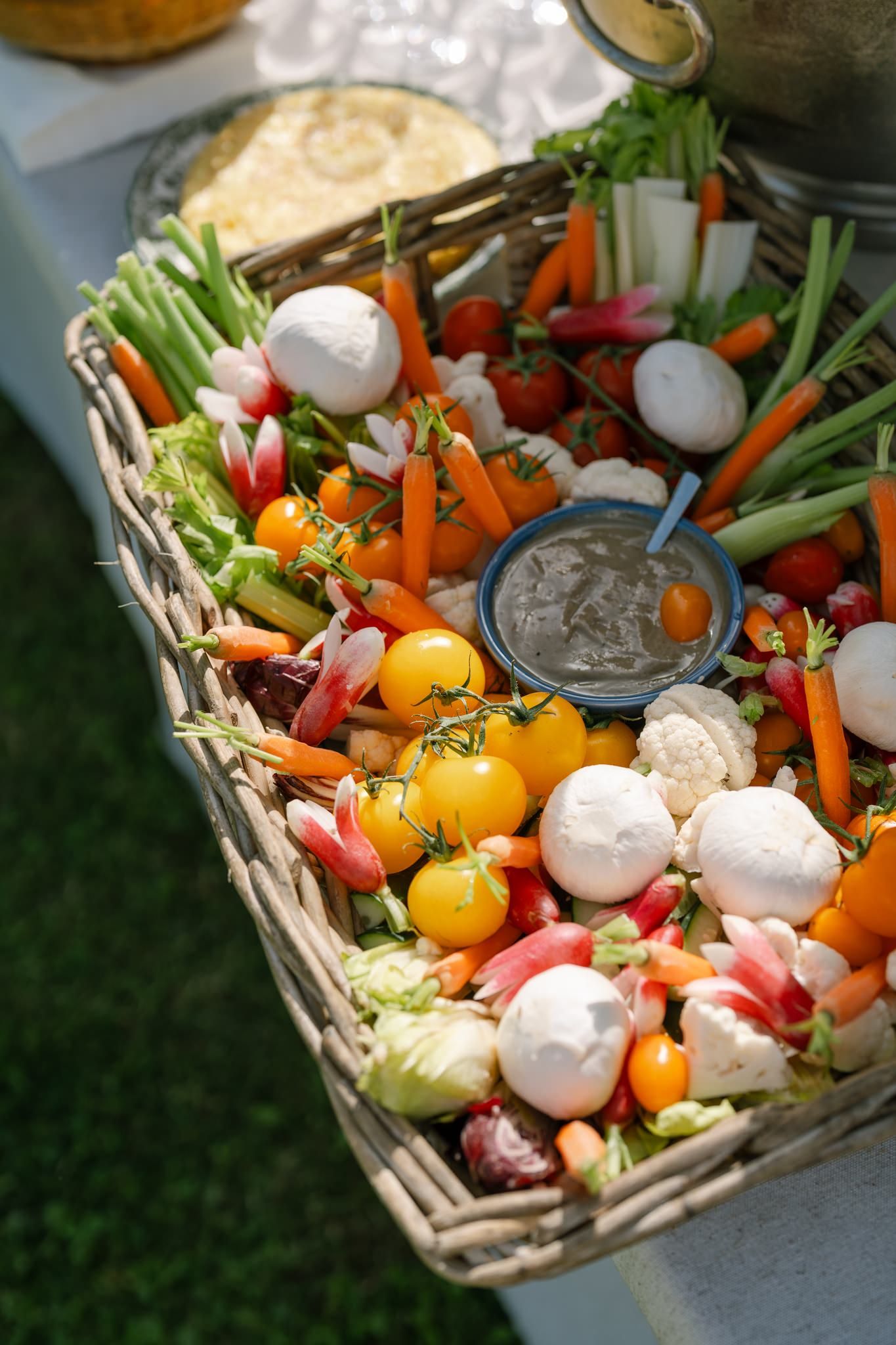 Fresh vegetable crudité platter with colorful carrots, radishes, and dip in a woven basket.