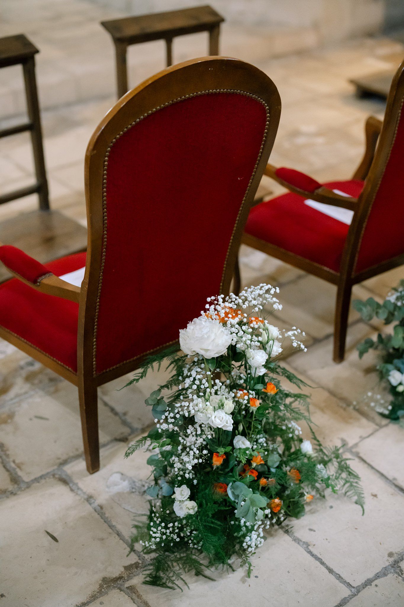 Elegant red velvet chair with floral arrangement featuring white flowers and greenery.