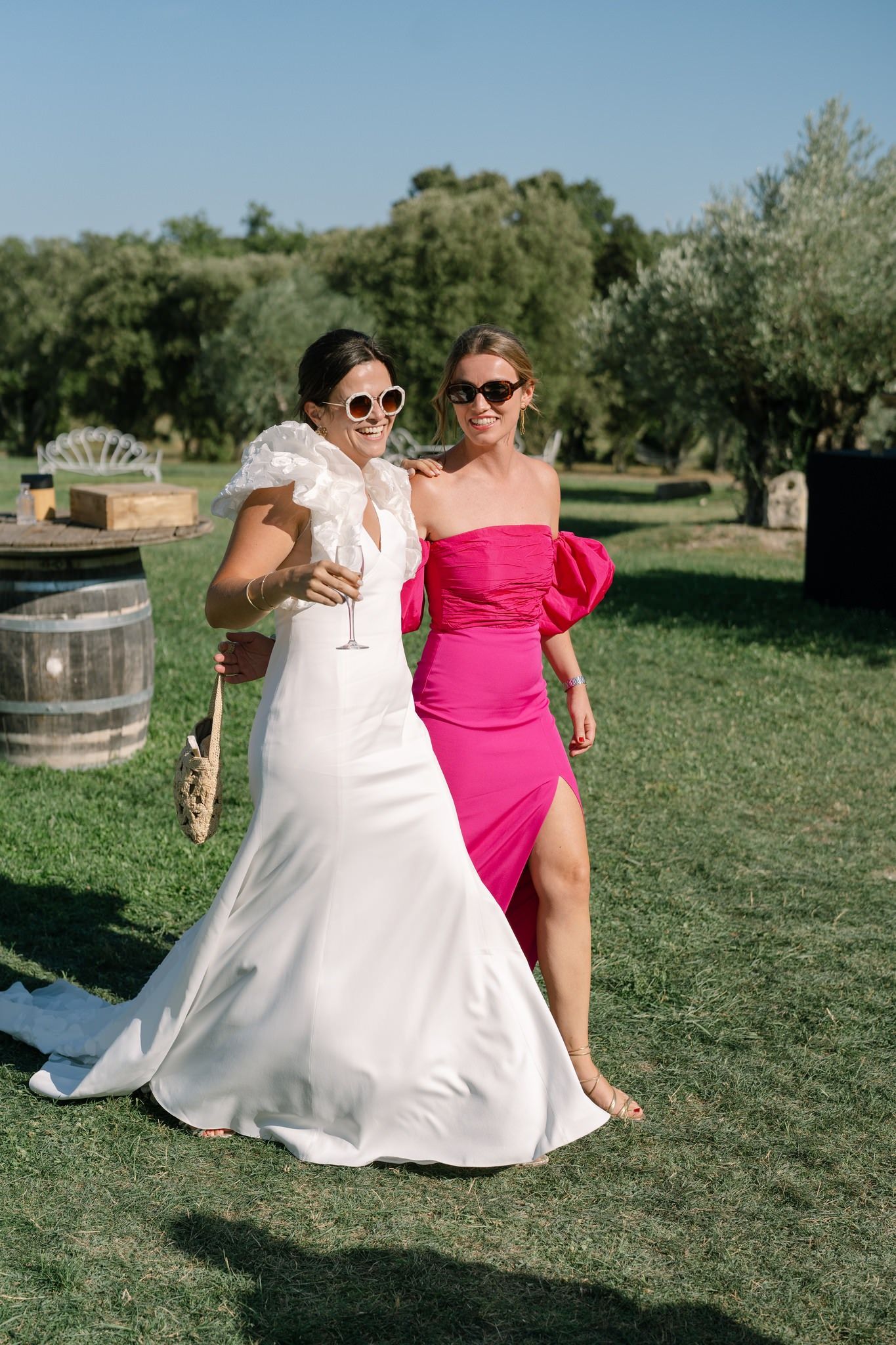 Wedding party in white and pink dresses posing on grassy lawn with decorative barrels.
