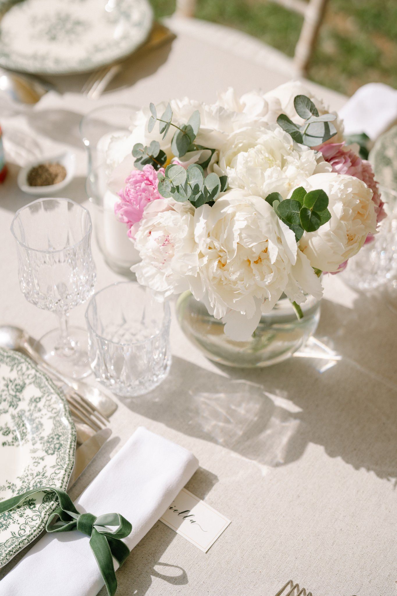 Elegant table setting with white peonies and crystal glassware on a light tablecloth.