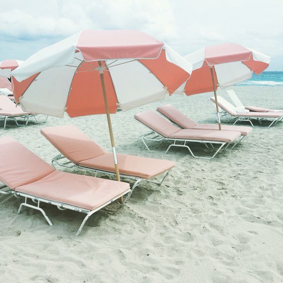 Row of pink beach loungers with white umbrellas on sandy beach.