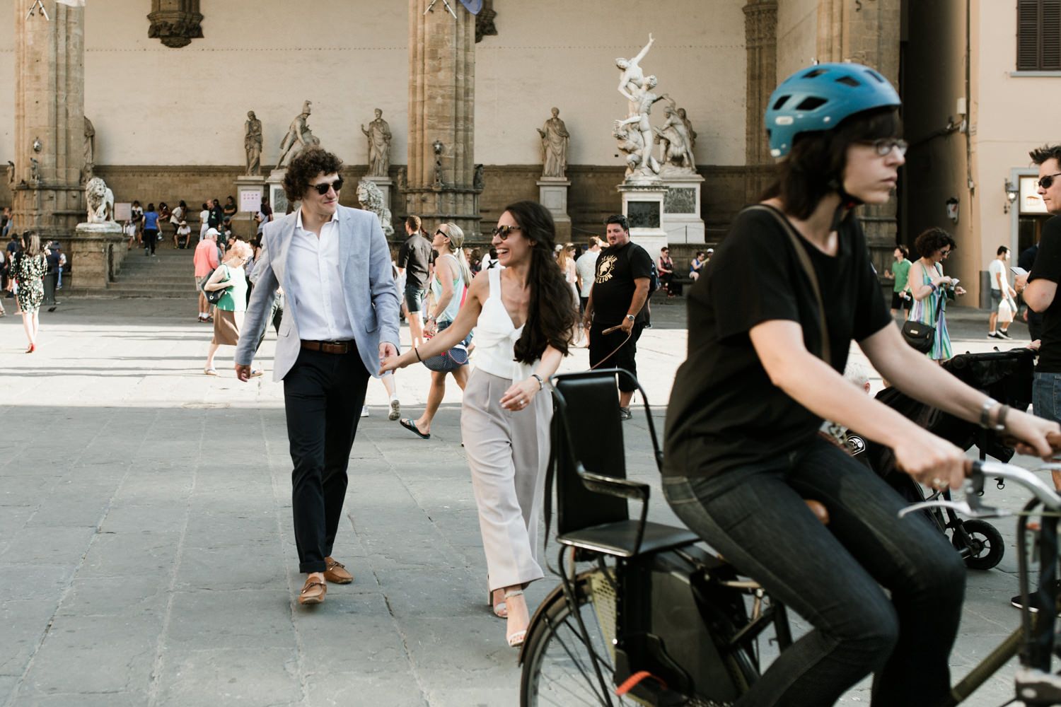Street scene in Florence with cyclists and pedestrians passing historic architecture.