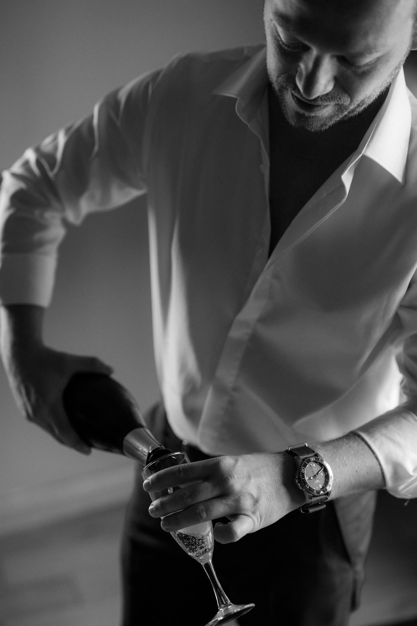 Person in white shirt pouring champagne in dramatic lighting.