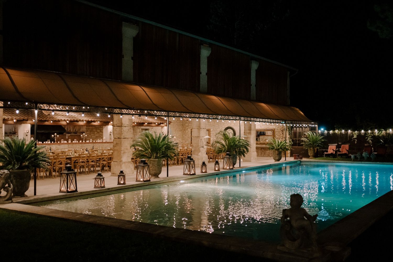 Illuminated swimming pool and reception area at night with string lights creating ambiance.