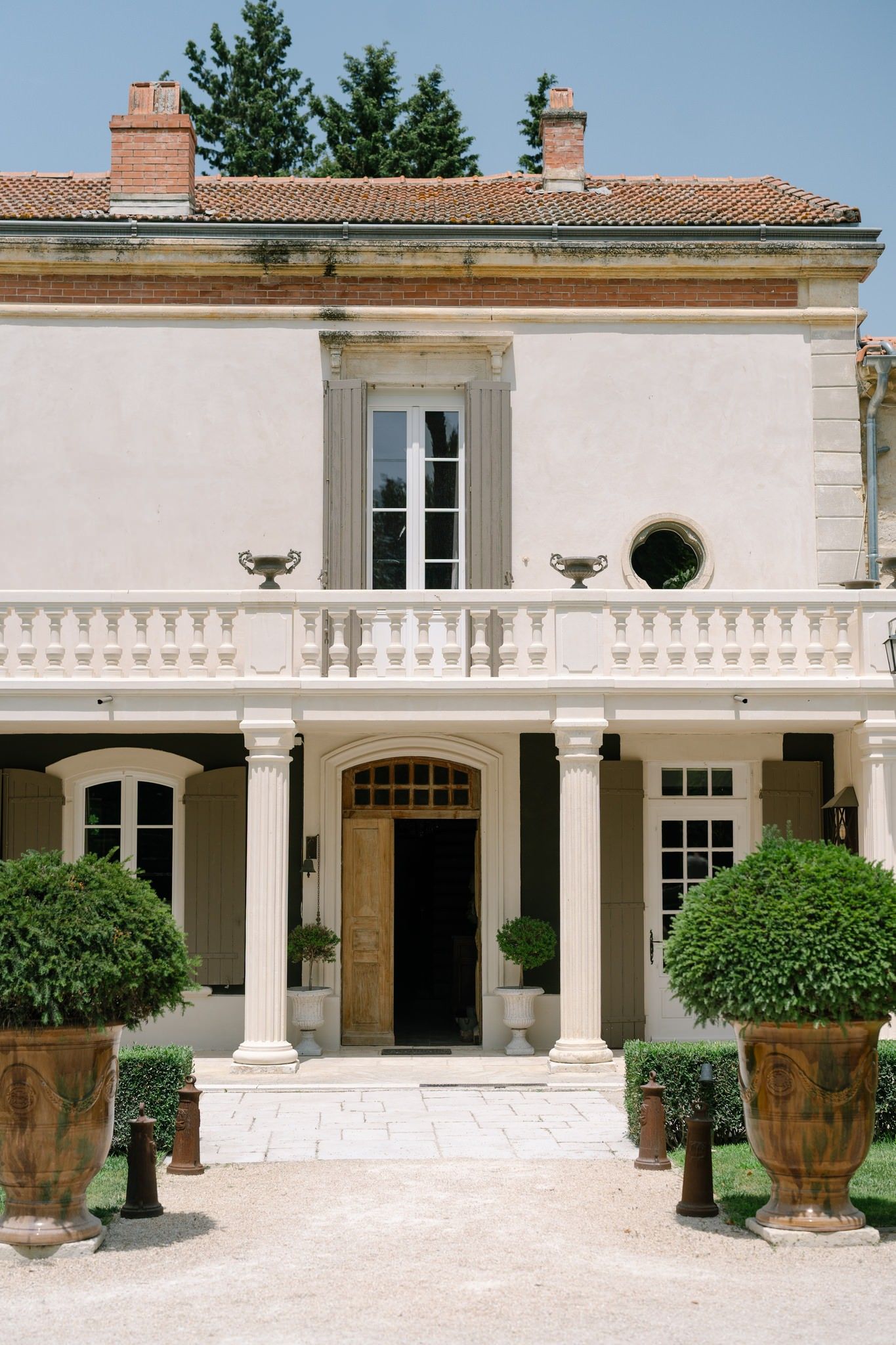 Elegant Mediterranean-style villa exterior with white columns, terracotta roof tiles, and large decorative urns flanking the entrance.