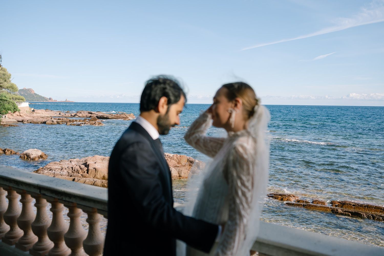A romantic seaside wedding photoshoot with a couple standing on a stone balcony overlooking the Mediterranean.