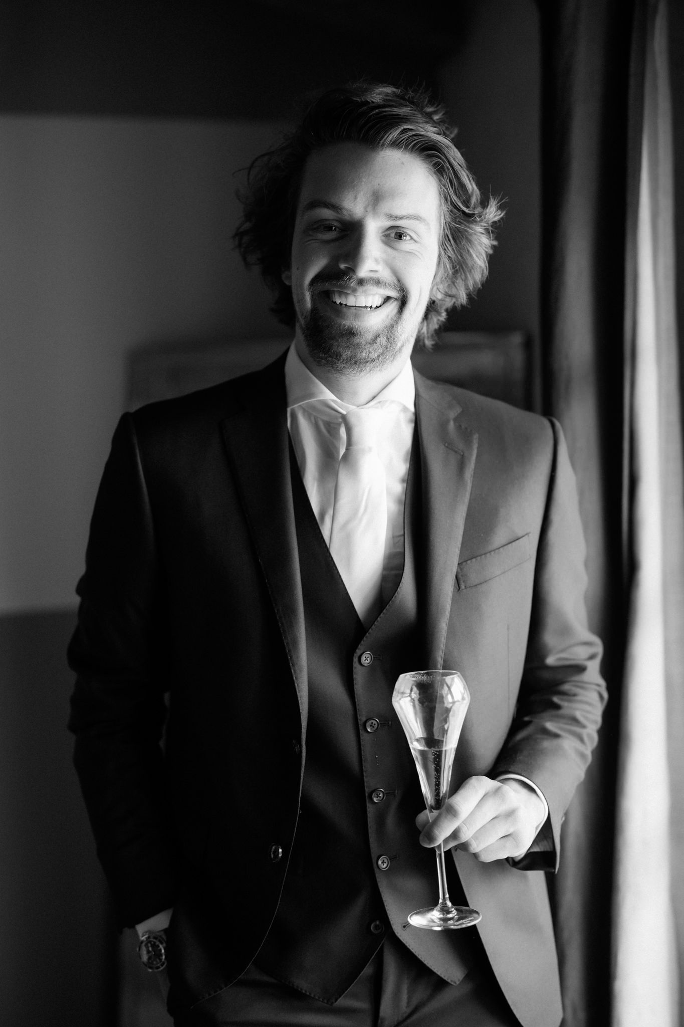 Black and white portrait of person in formal suit holding champagne glass.