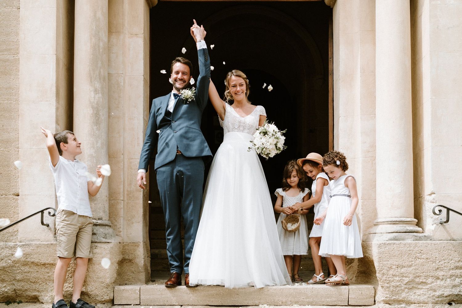 Wedding party gathered at an elegant stone archway entrance for formal photographs.