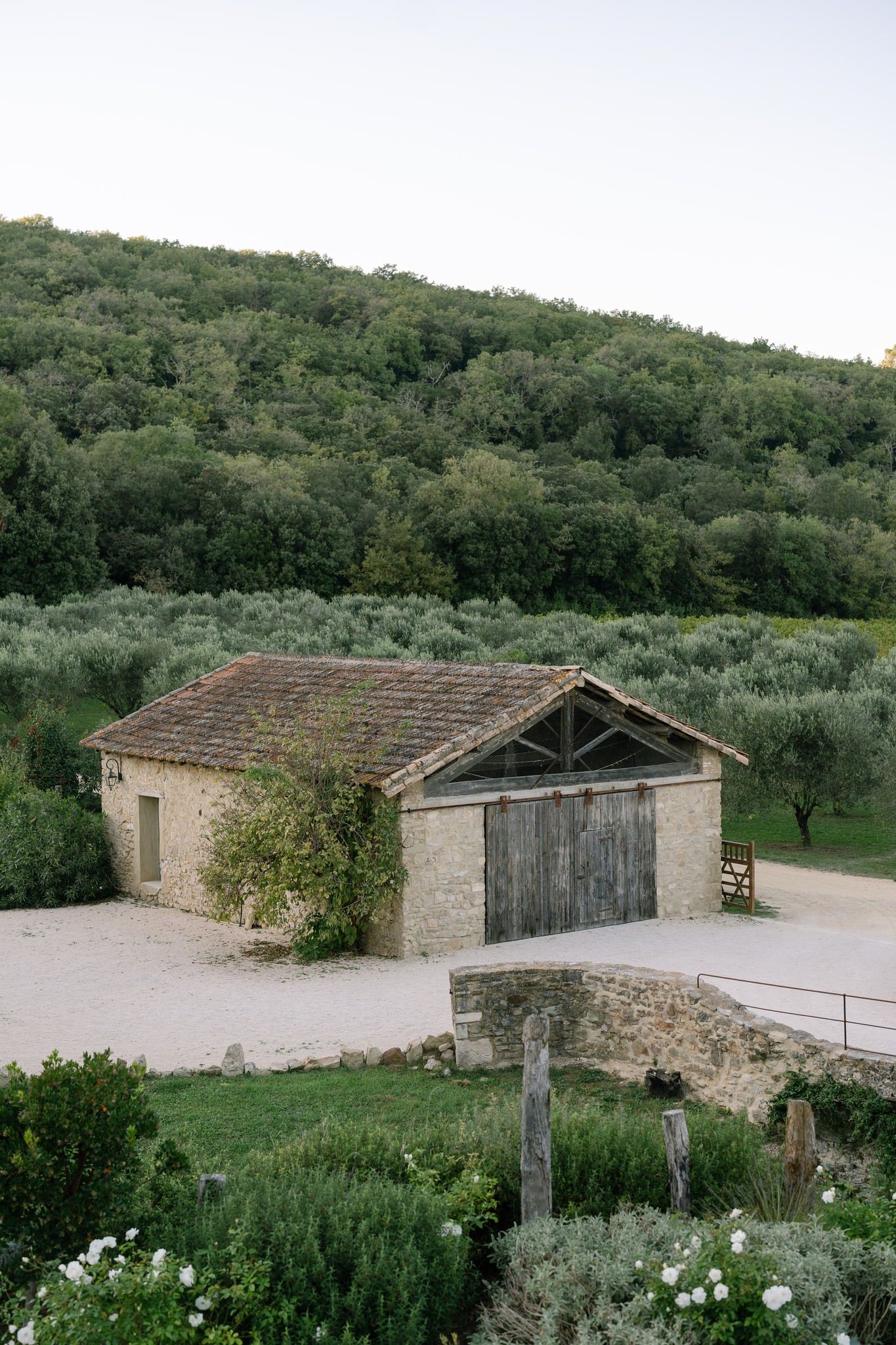Stone farm buildings with wooden doors nestled in a green hillside landscape.