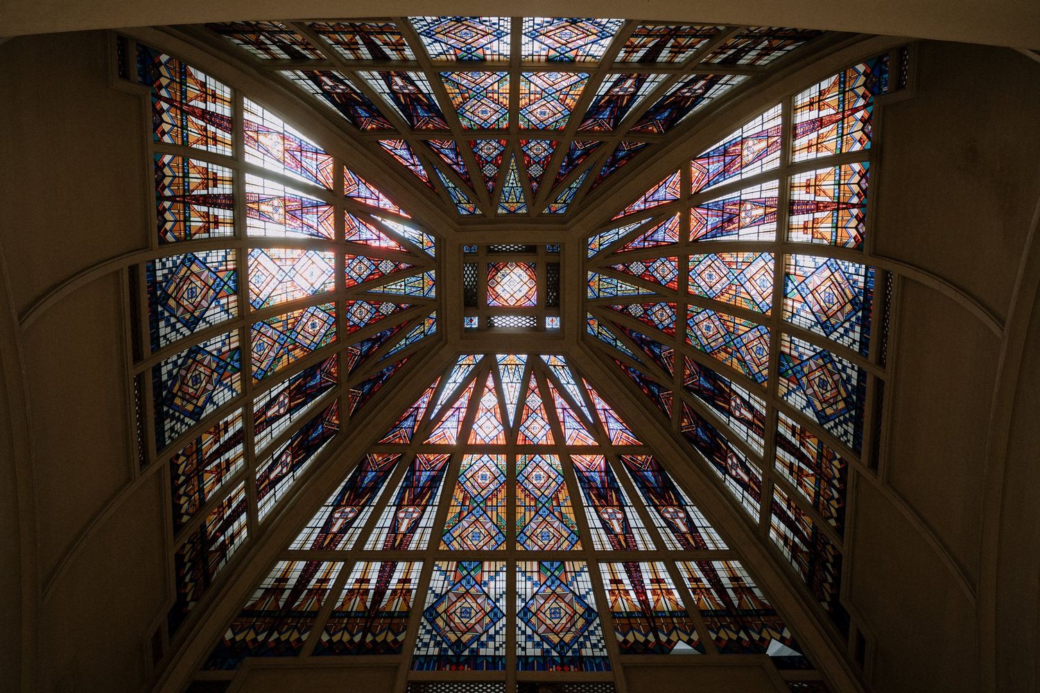 Stunning upward view of ornate stained glass cathedral ceiling with intricate geometric patterns and decorative details.