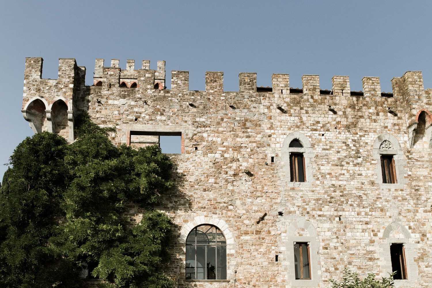 Historic stone castle walls with medieval architecture and windows against a blue sky.
