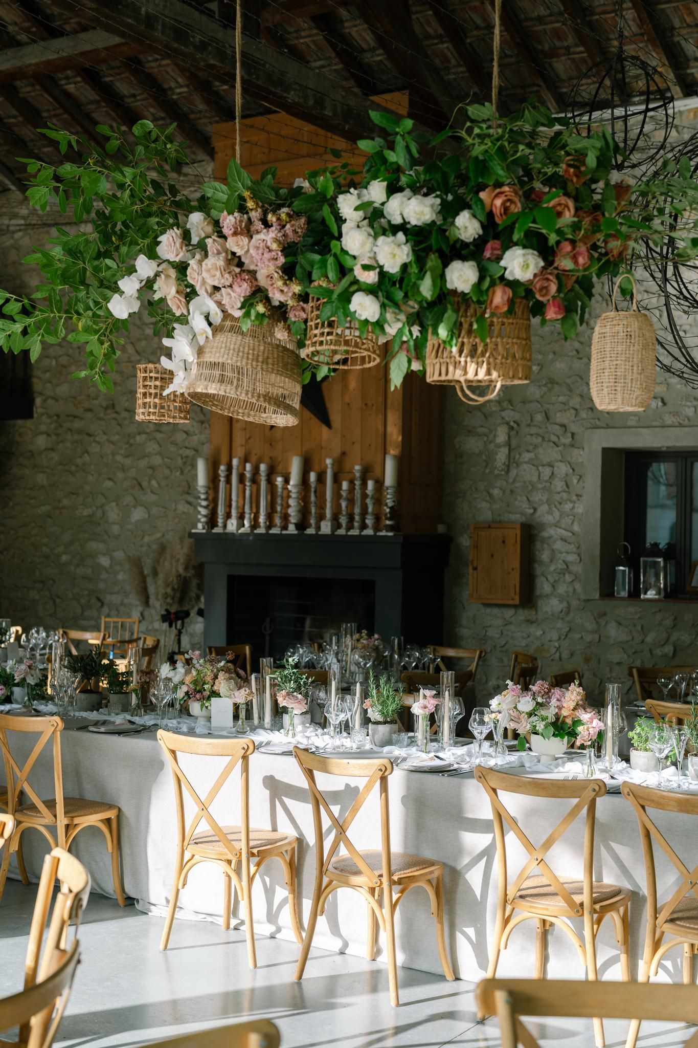 Elegant wedding reception venue with rustic stone walls, wooden chairs, and floral chandeliers.