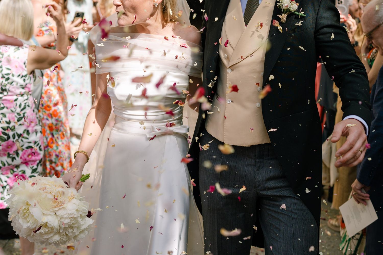 Newlywed couple walking through colorful confetti shower after wedding ceremony outdoors.