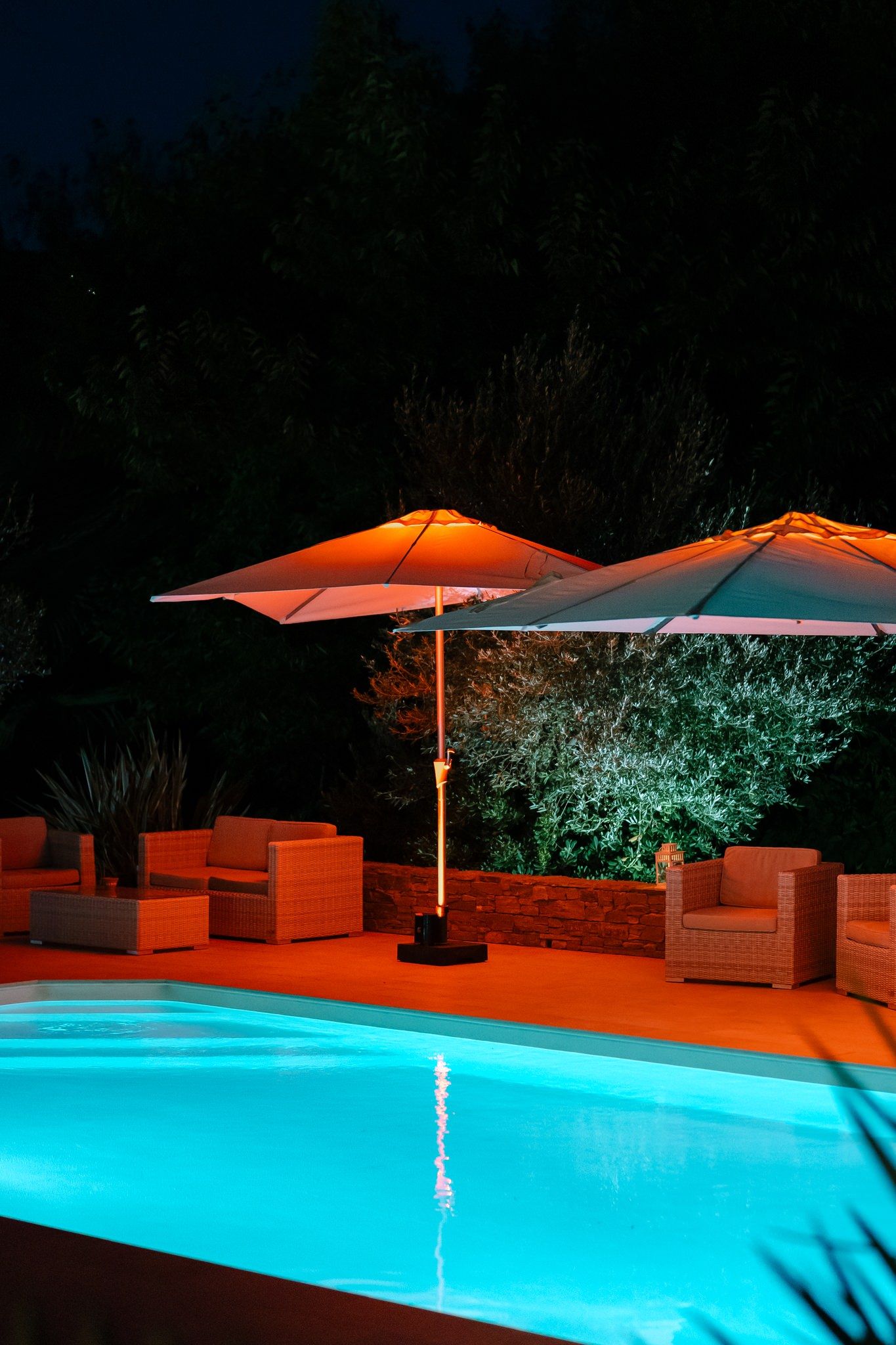 Illuminated swimming pool with orange umbrellas and turquoise lighting at night.