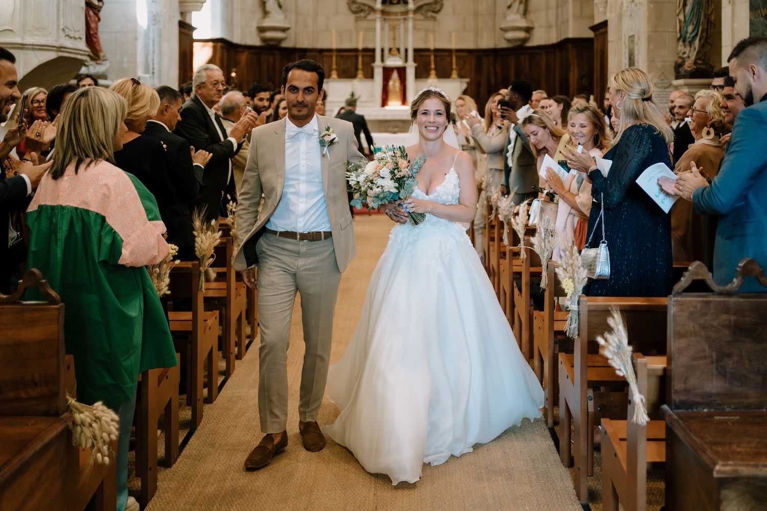 A wedding ceremony recessional in a traditional church with guests lining the aisle.