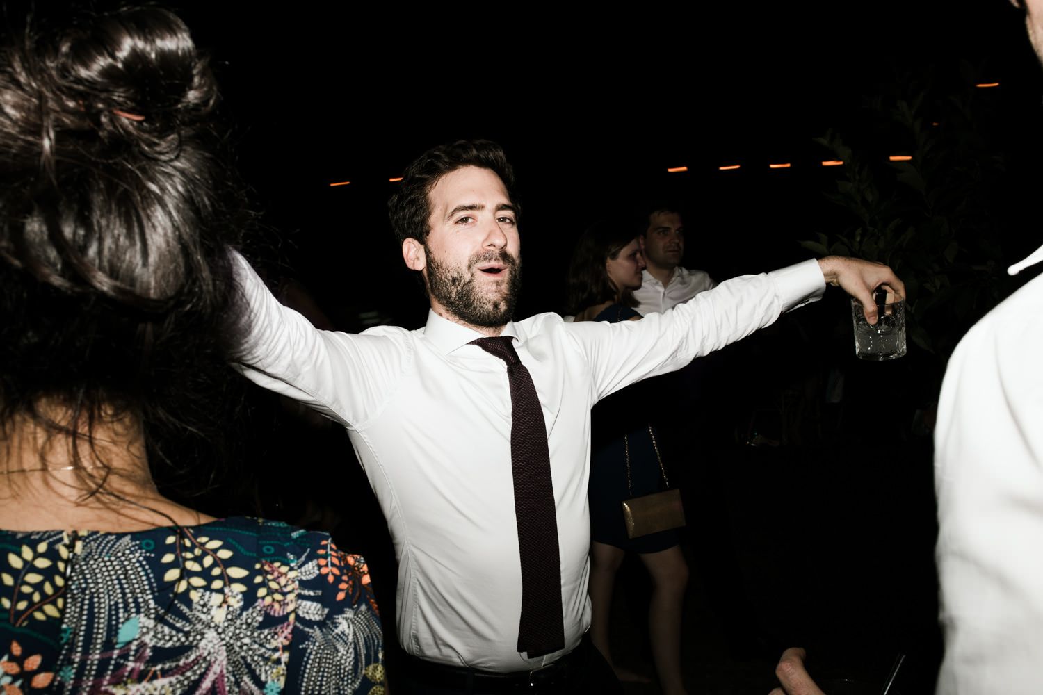 Wedding reception guests dancing and celebrating on a dark dance floor with dramatic lighting.