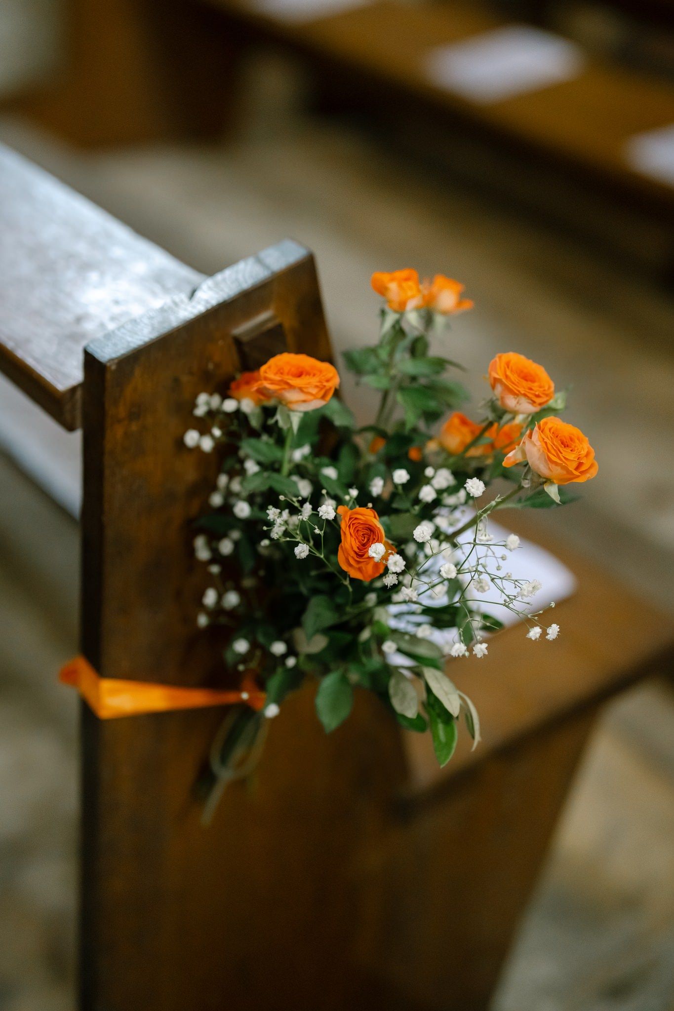 Orange roses and baby's breath flowers decorating wooden church pews.