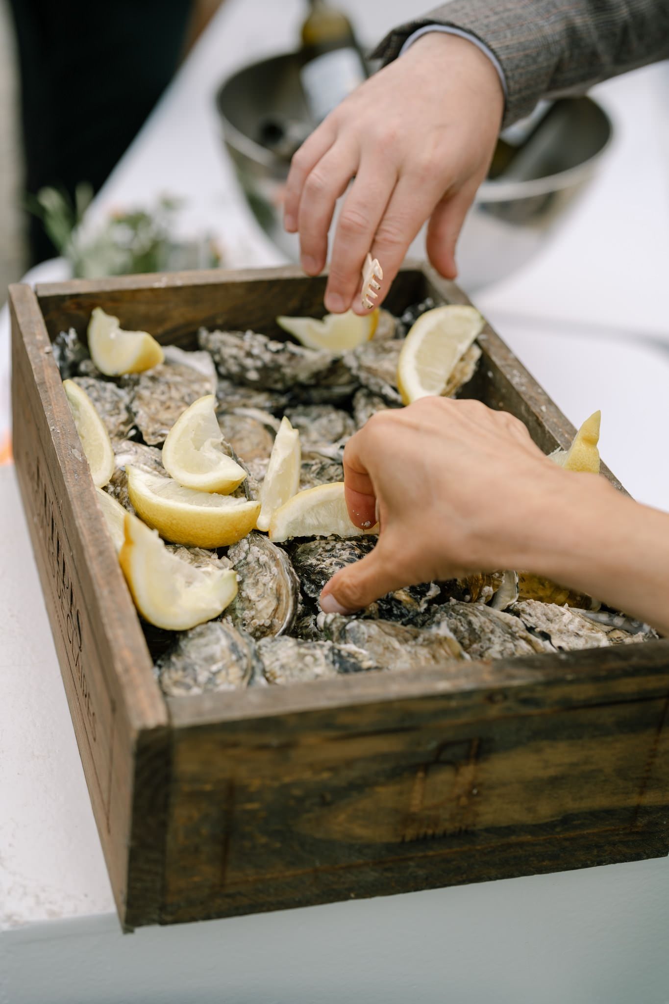 Fresh oysters being served on ice in a rustic wooden box with lemon wedges.