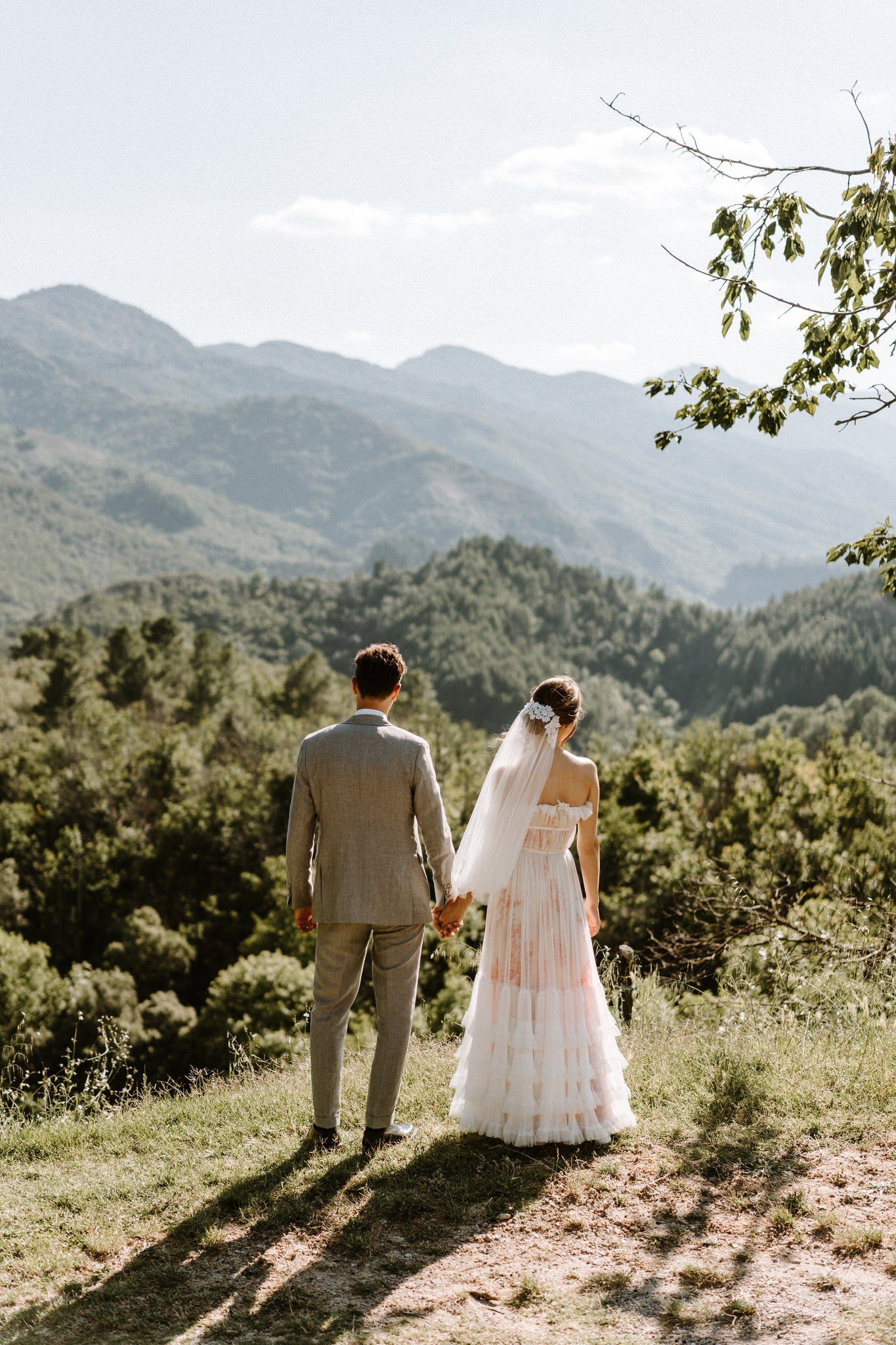 A couple in wedding attire stands together overlooking a scenic mountain landscape on their special day.
