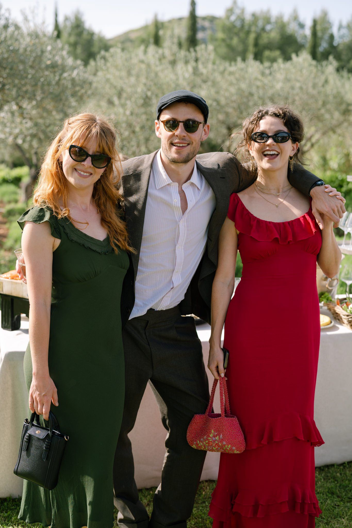 Wedding guests in formal attire posing together outdoors among olive trees.