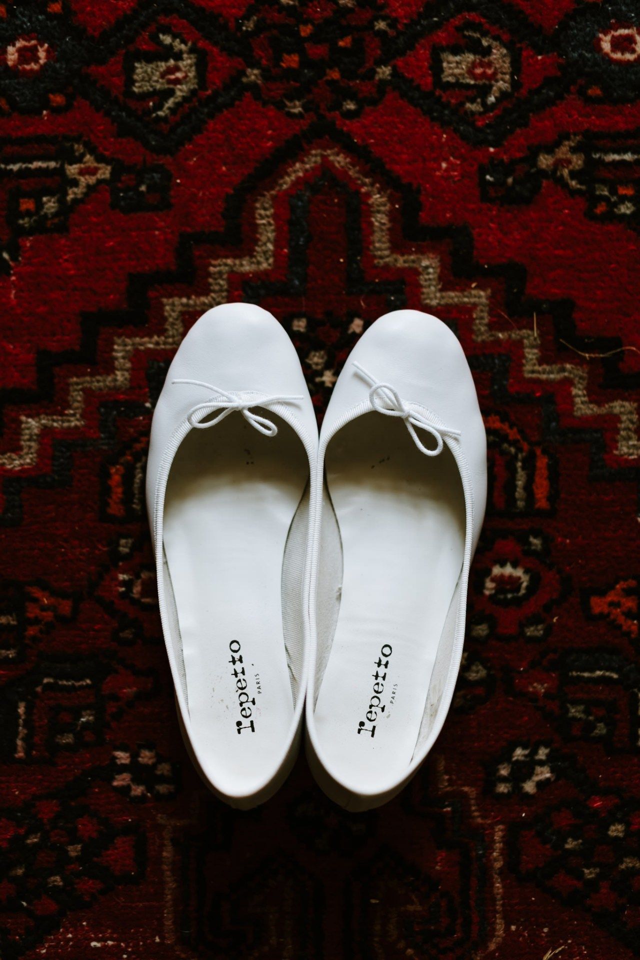 White bridal shoes displayed on a dark red patterned carpet.