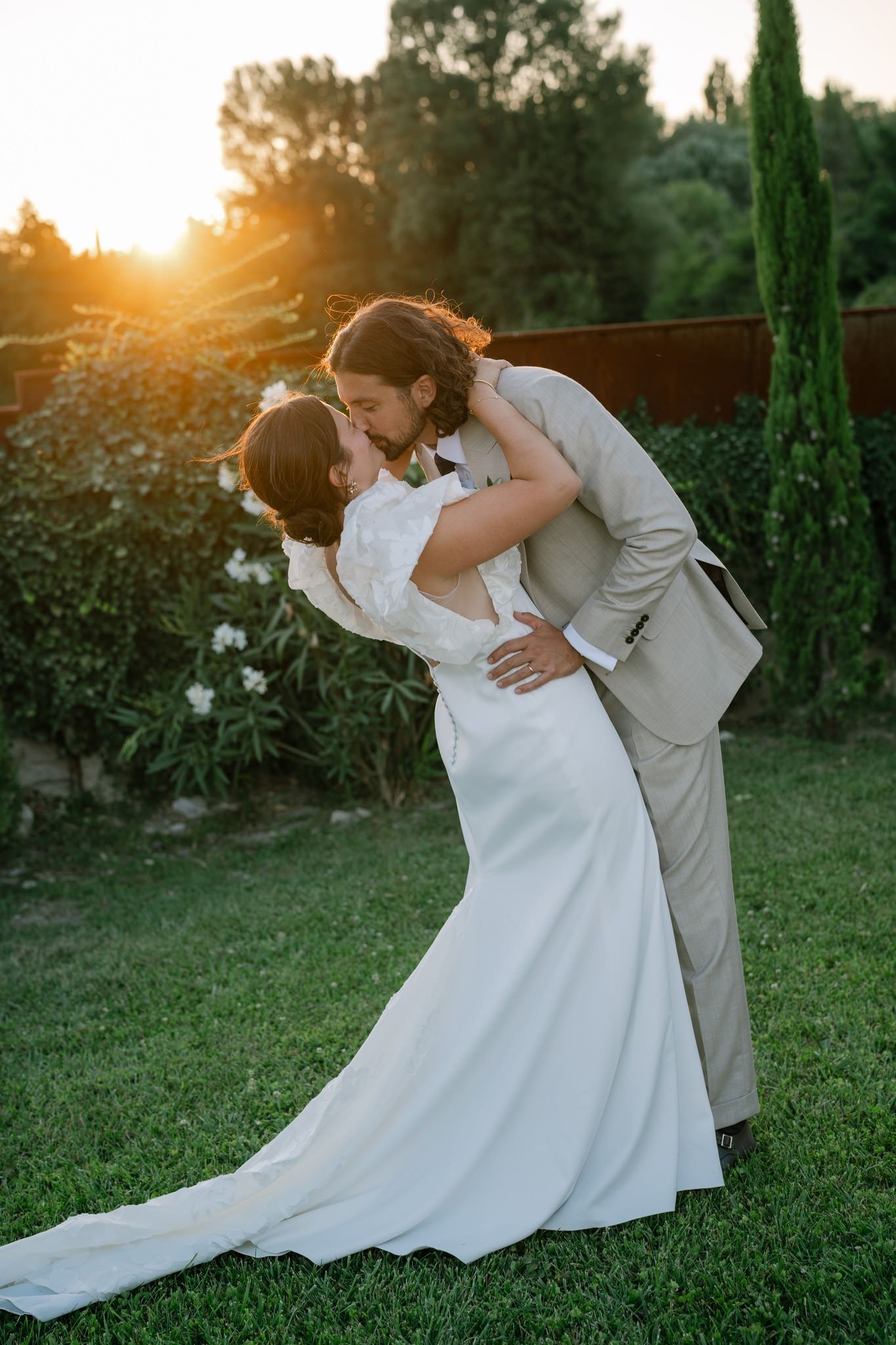 Romantic sunset wedding portrait with couple embracing on garden lawn.