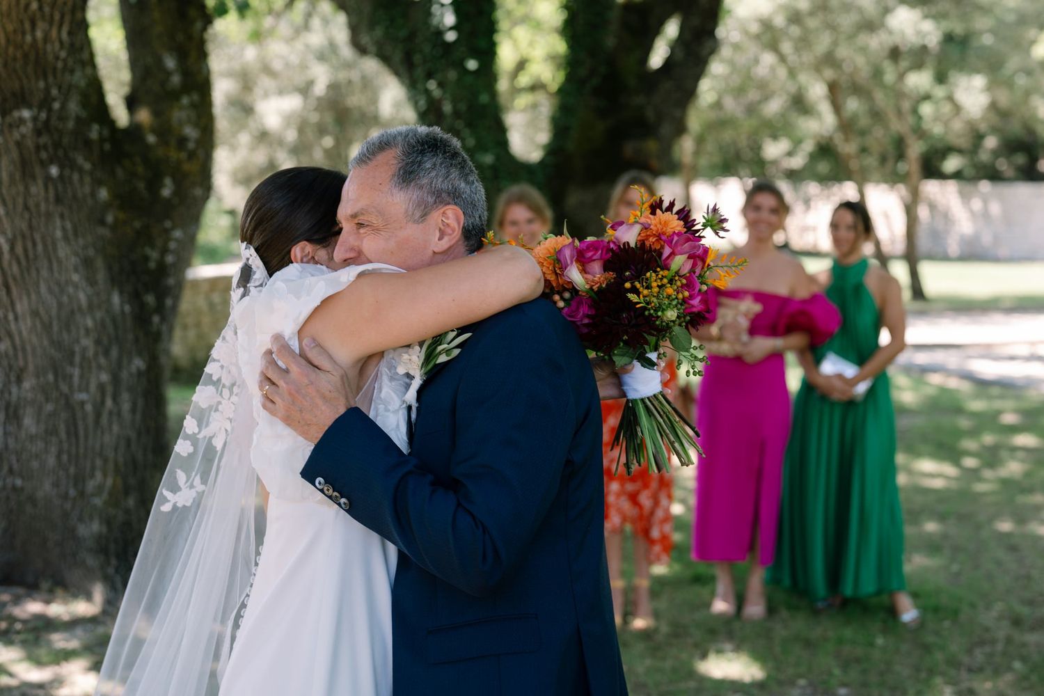 Emotional wedding moments captured under trees with family and guests in formal attire.
