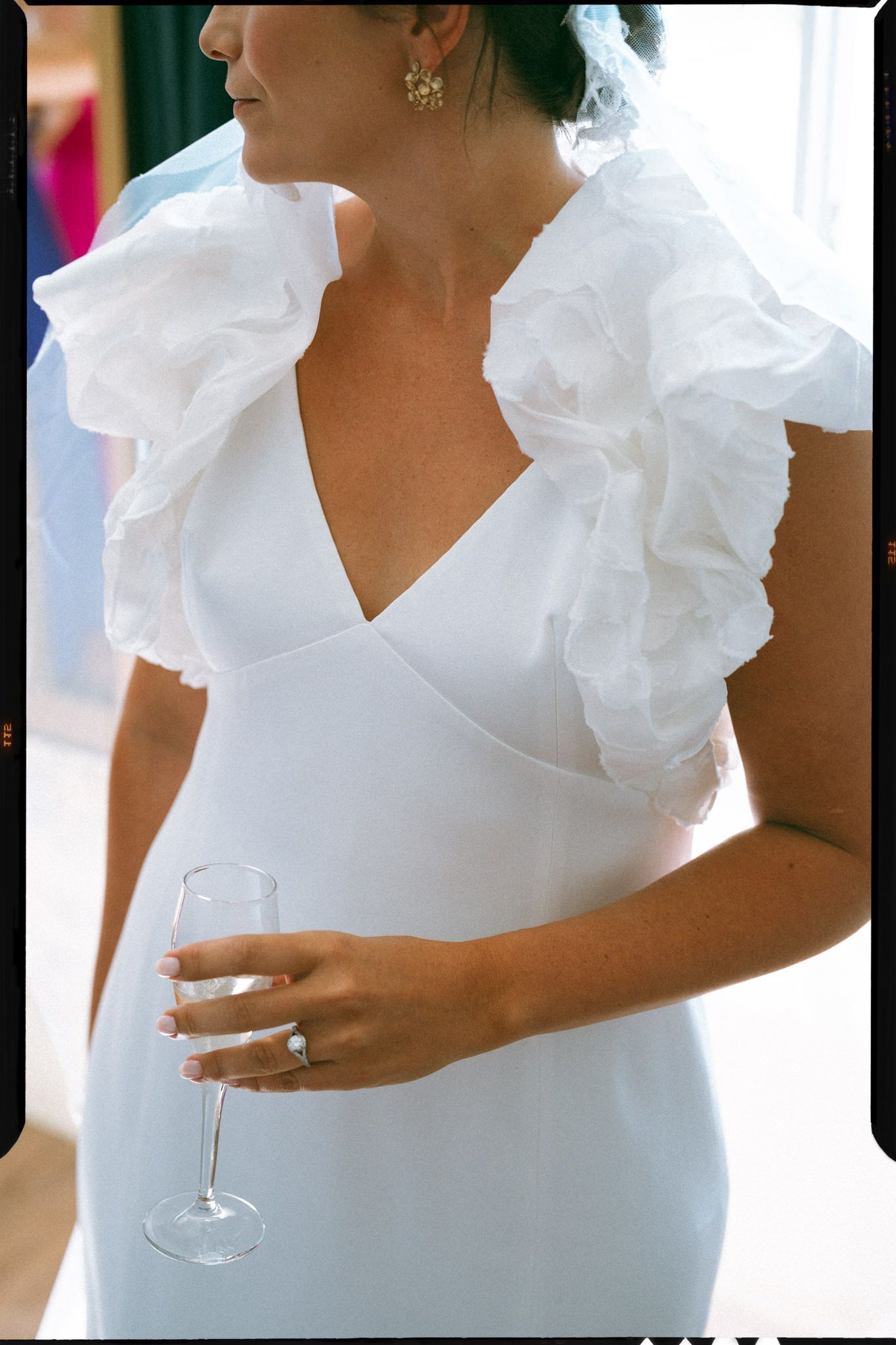 A close-up view of a white ruffled neckline dress with someone holding a wine glass against a light background.