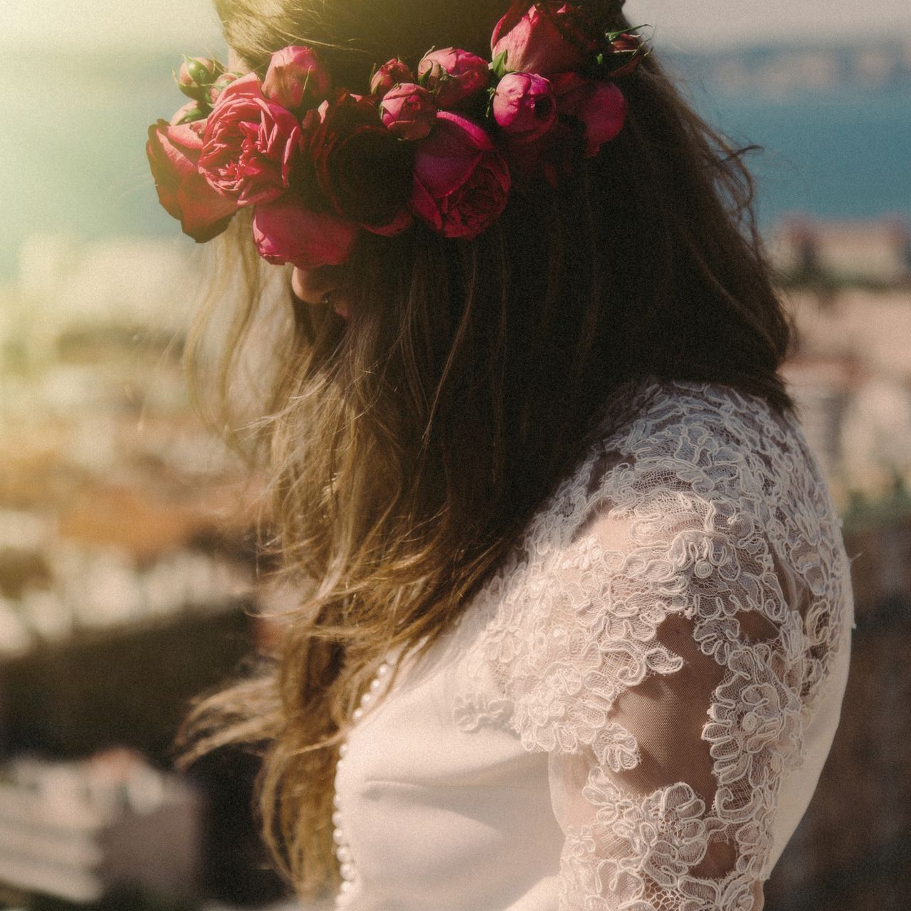 Close-up details of a bride's lace dress and floral crown with pink roses.