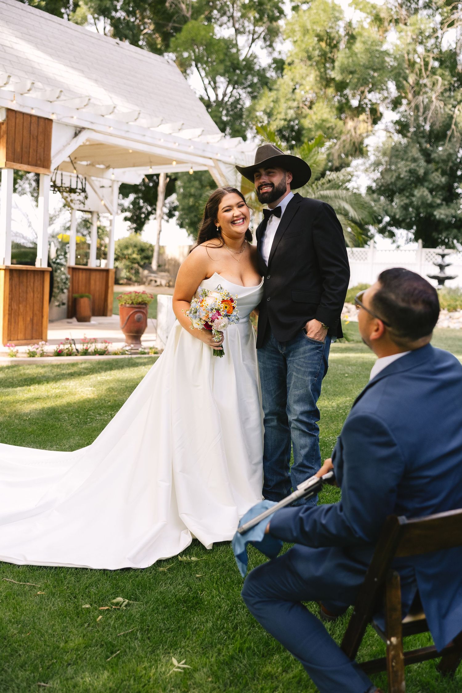 Rustic outdoor wedding ceremony at a charming white gazebo venue with wooden accents and lush green landscaping.