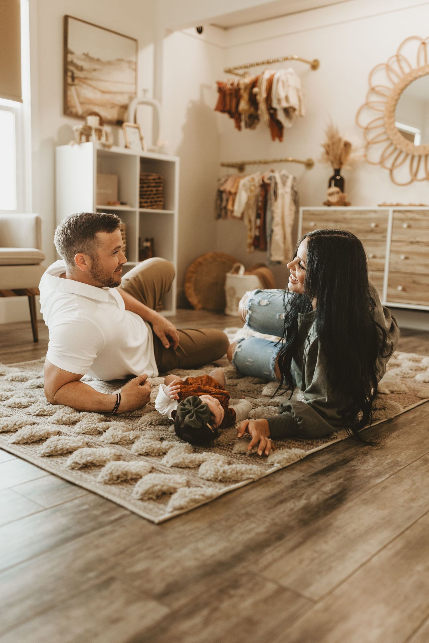 Cozy nursery scene with two people sitting on a patterned rug surrounded by baby decor.