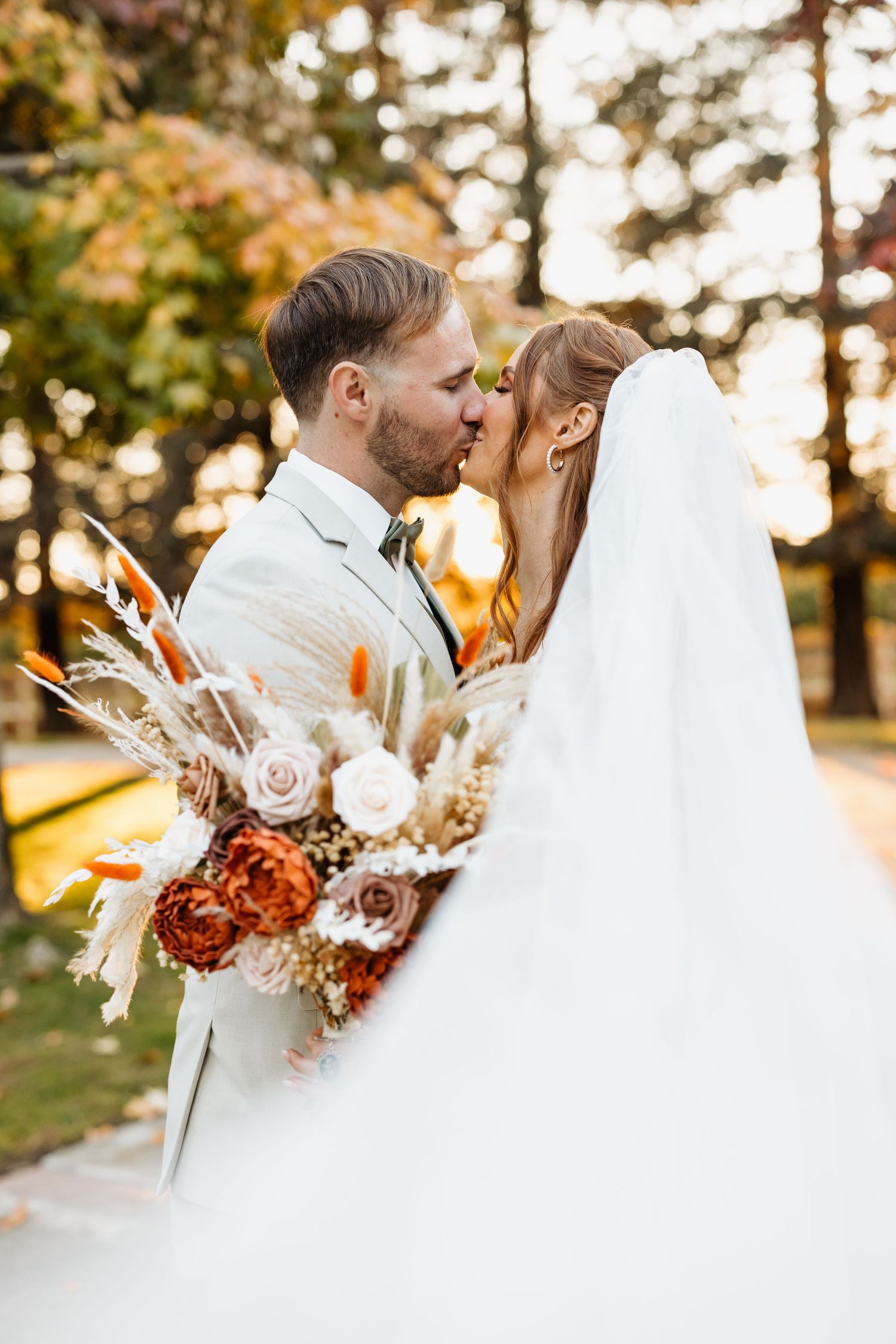 Romantic autumn wedding photo with flowing veil and bouquet of roses and dried flowers at sunset.