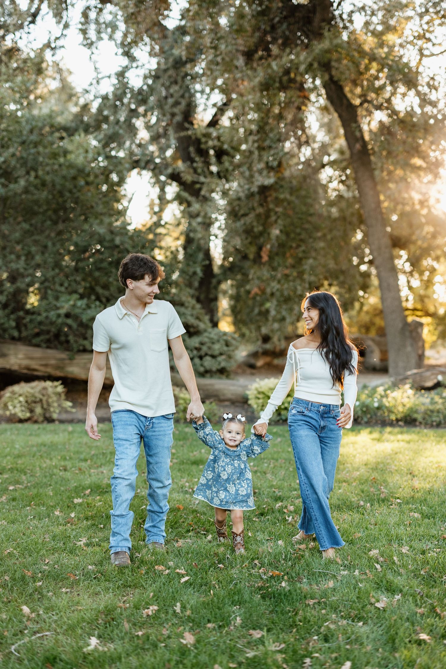 A family holding hands while walking together on grass in a sunlit park during golden hour.
