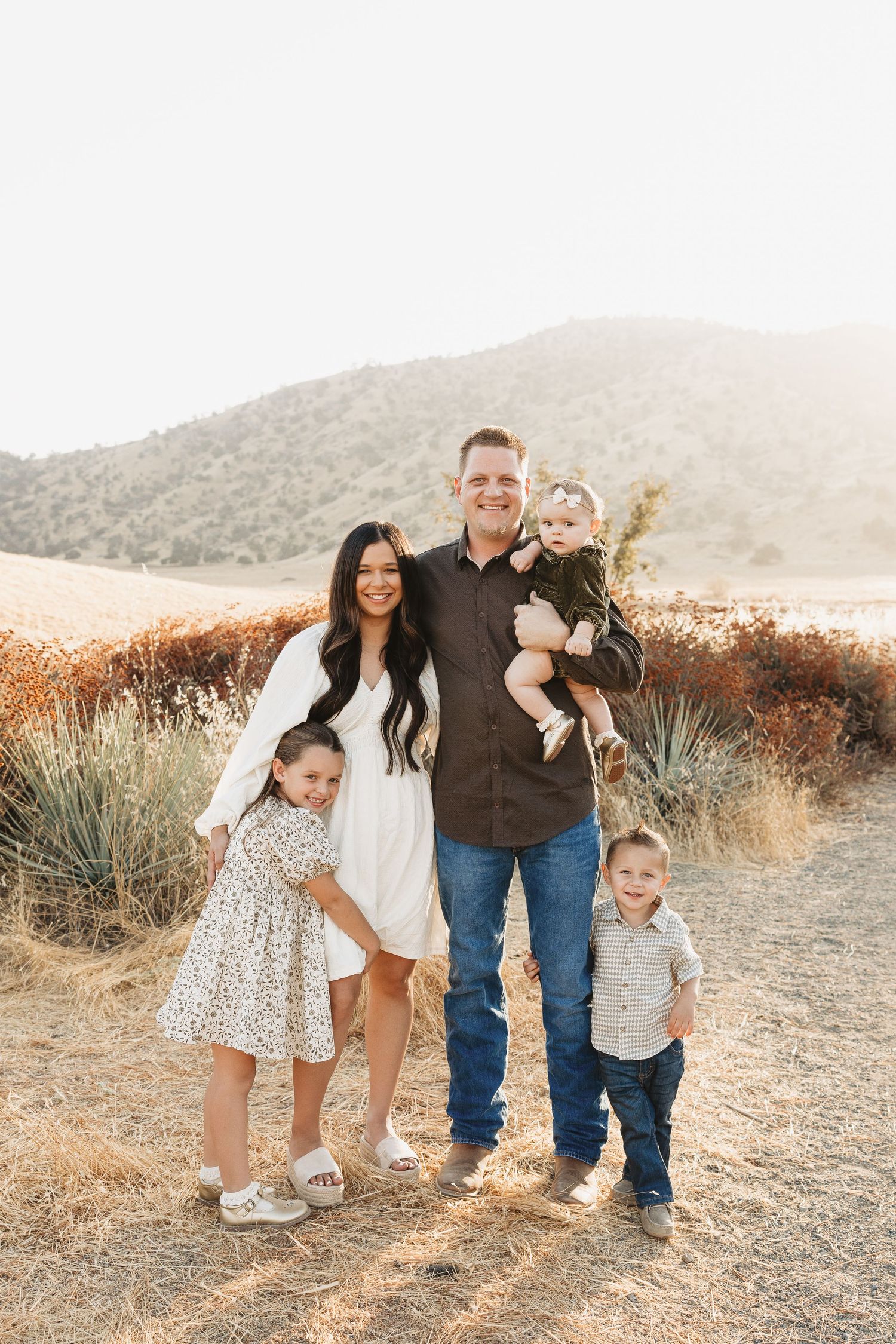 Family portrait in golden sunset light among desert brush and rolling hills.