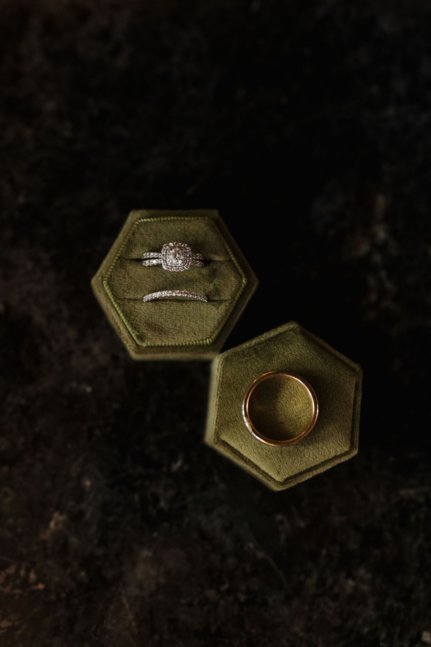 Wedding rings displayed in olive green velvet hexagonal ring boxes on dark background.