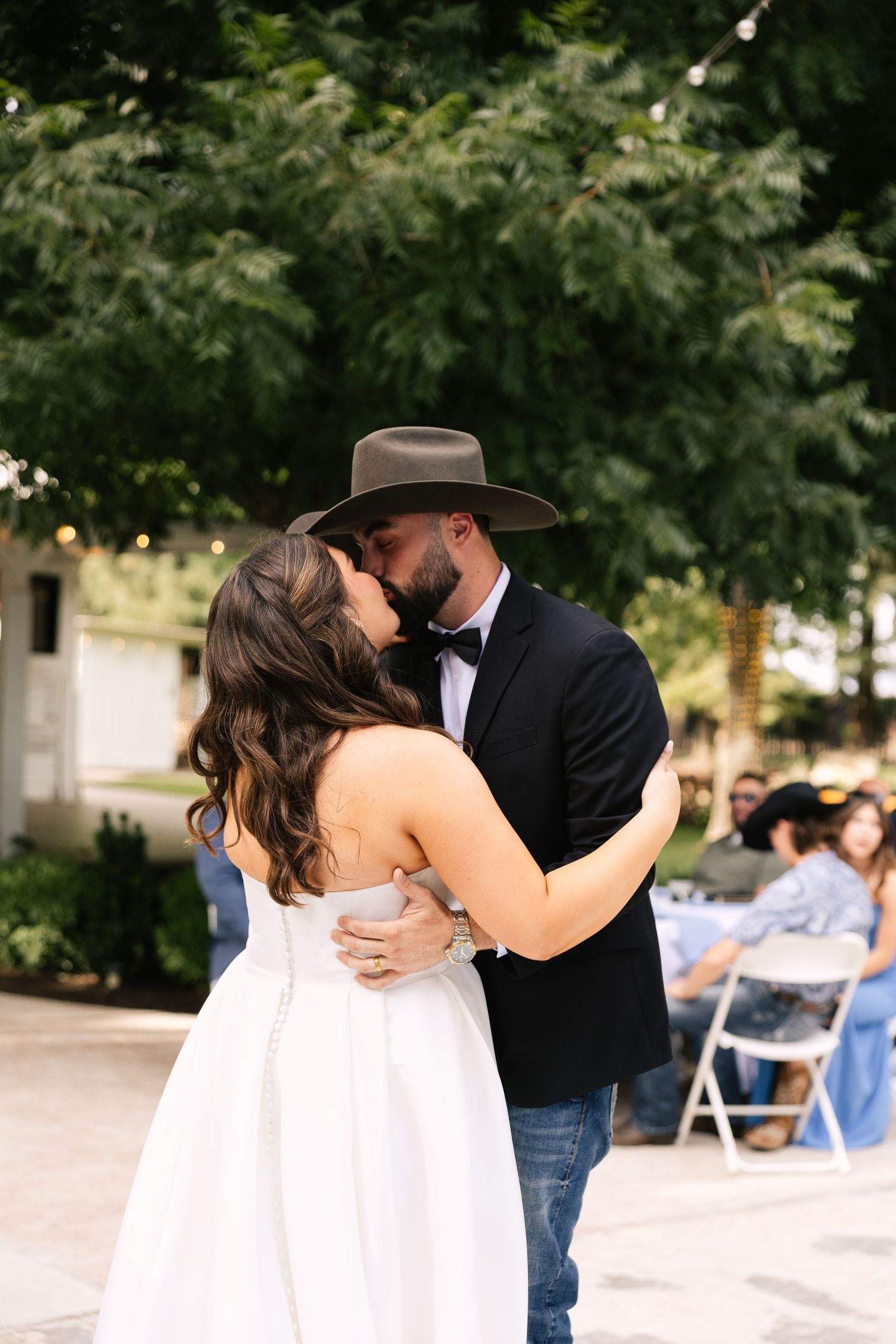 A couple shares a romantic dance at an outdoor wedding reception with string lights and trees in the background.