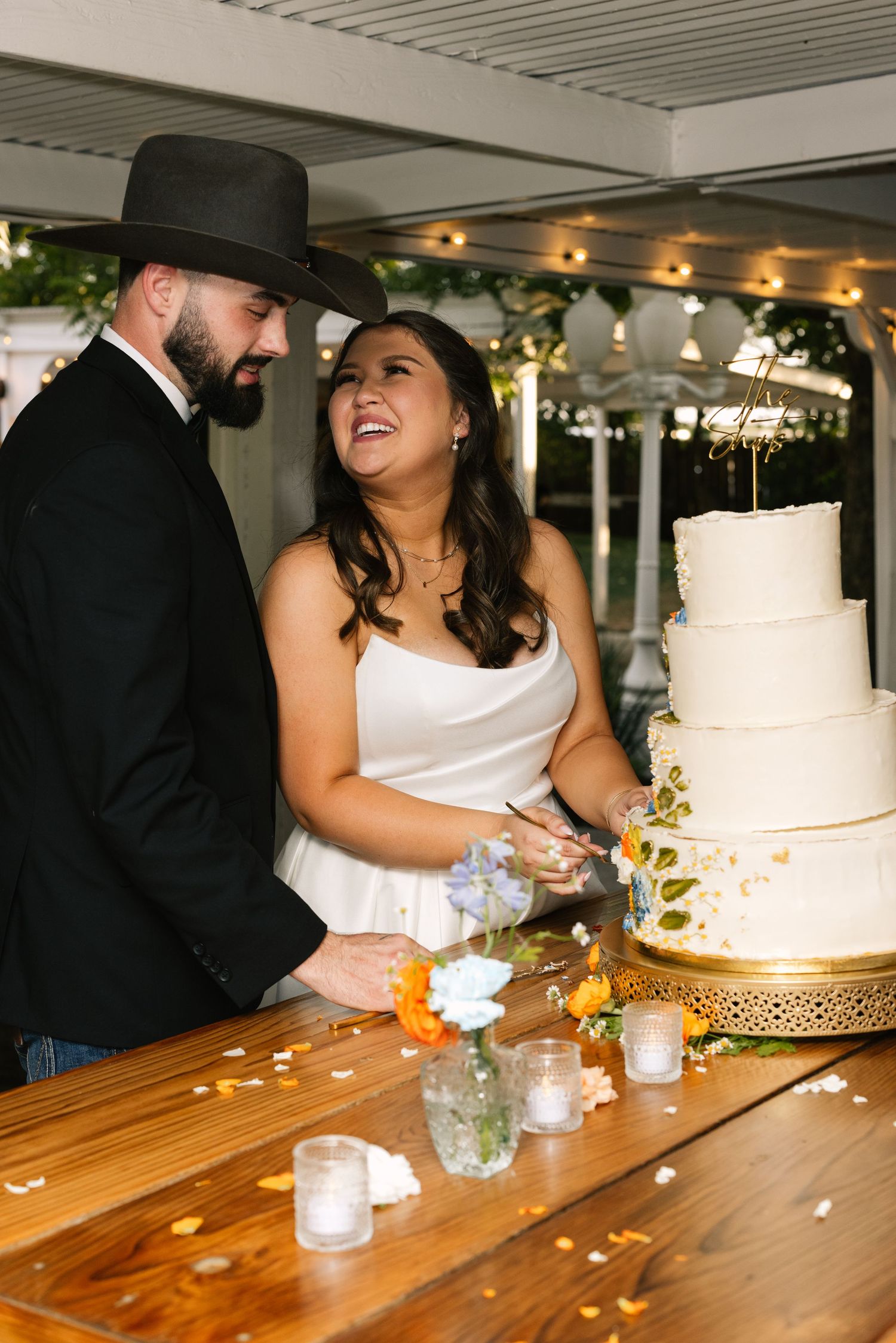 A joyful wedding cake cutting moment at a rustic reception with a white tiered cake on a wooden table.