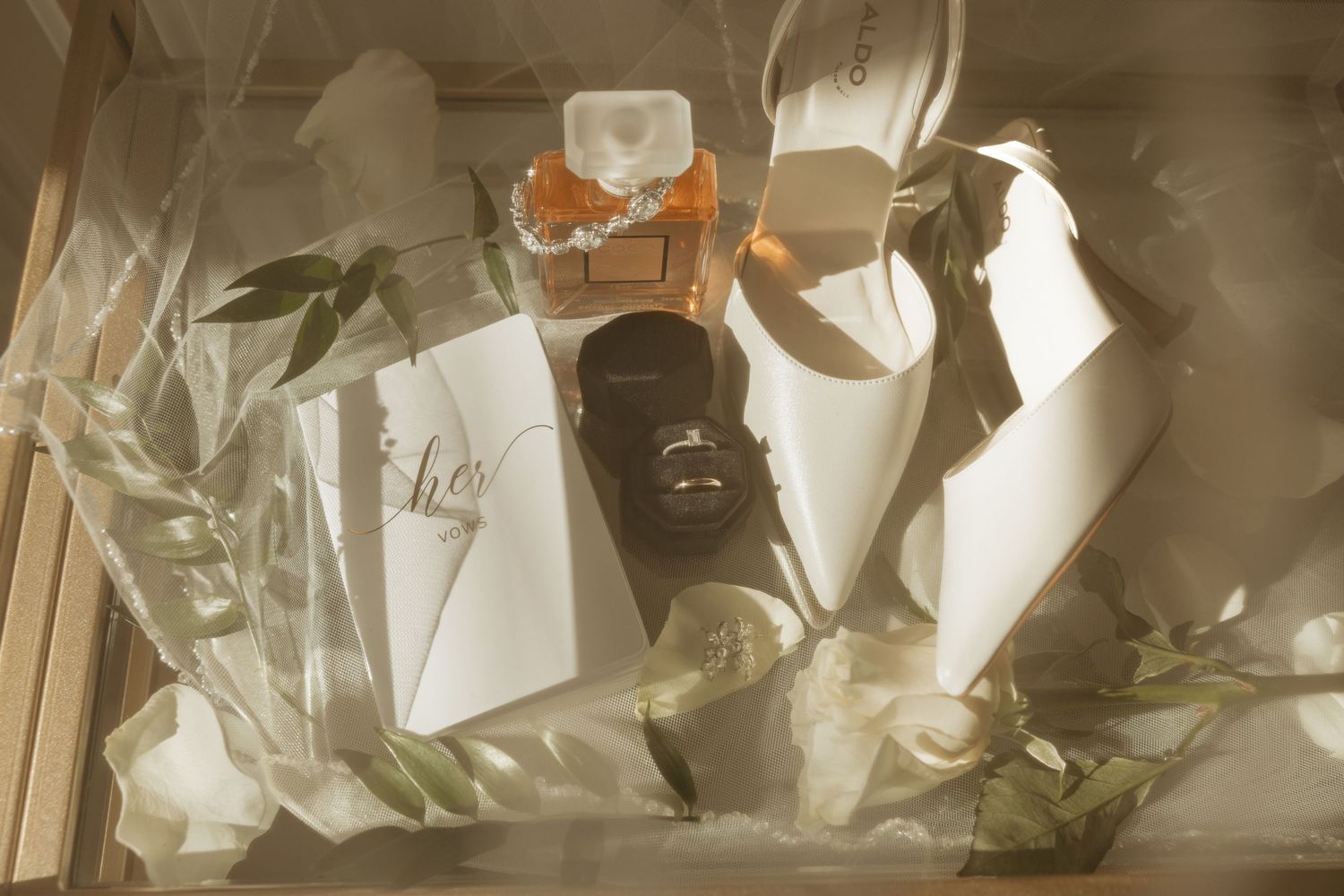 A bottle of bitters with orange accents sits in moody lighting surrounded by greenery and glassware.