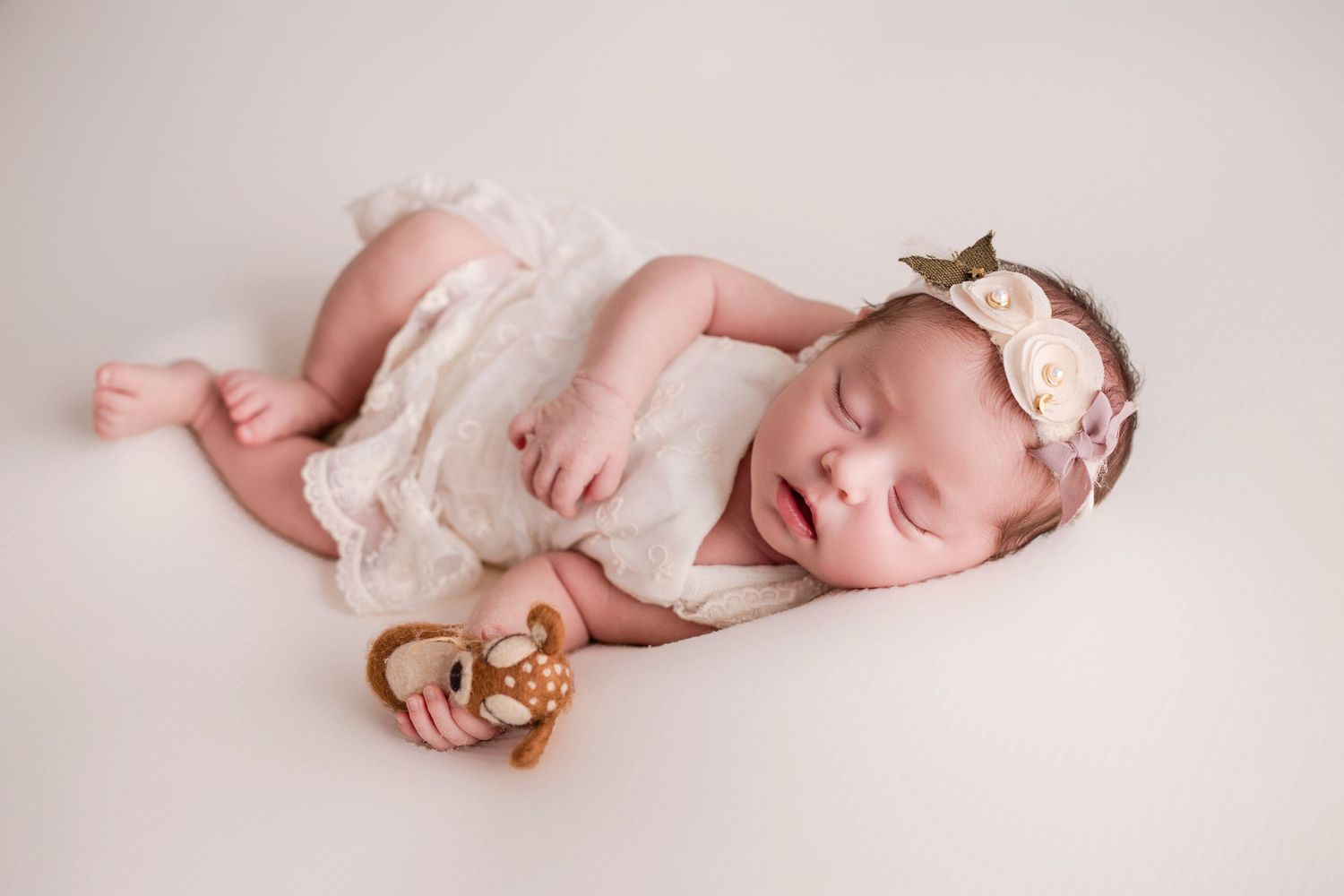 Peaceful newborn baby sleeping in soft pink tones while wrapped in delicate fabric during professional photography session.