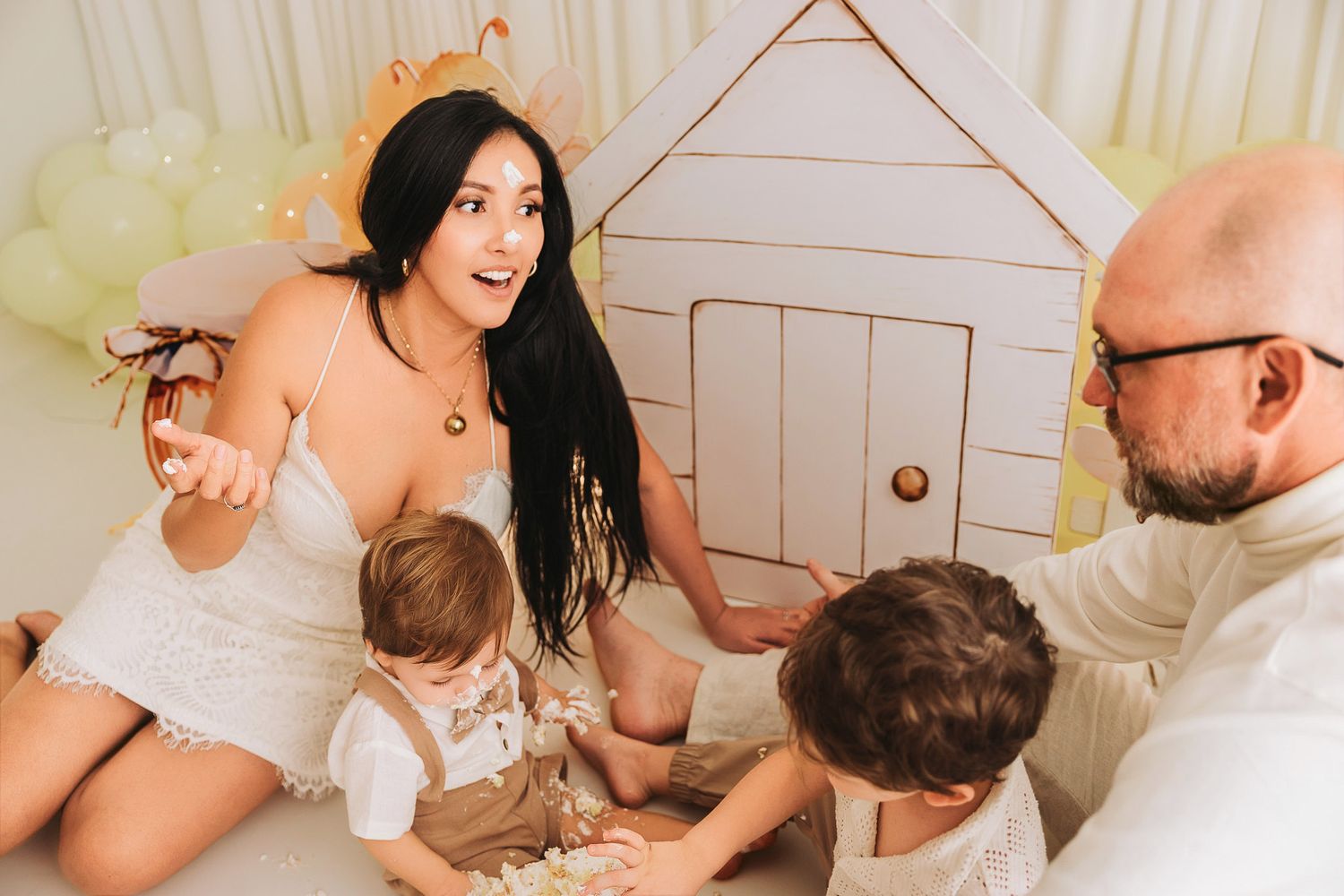 Family of four enjoying playtime together near a decorative cardboard house with balloons in a bright, cozy setting.