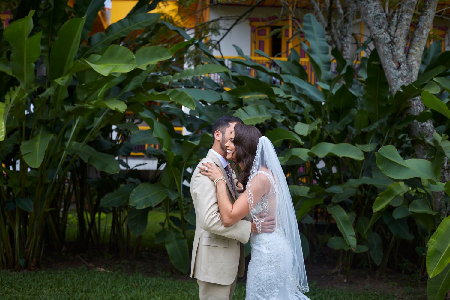 Bride and groom kiss in a lush tropical garden setting surrounded by green foliage.