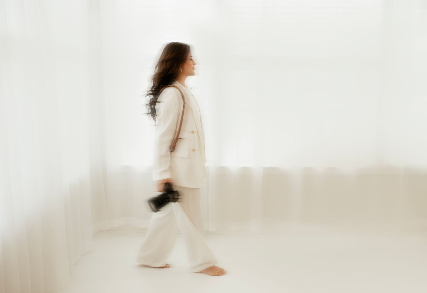 Motion blur of person walking with camera in white minimalist setting.