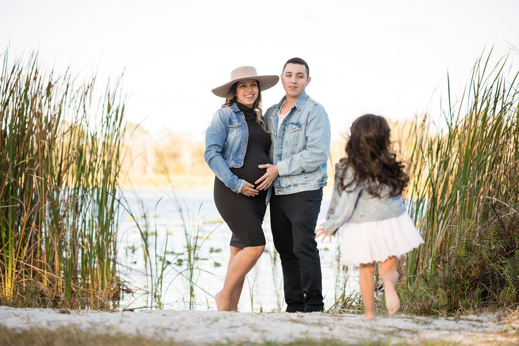 Family maternity photo at lakeside with reeds during sunset.