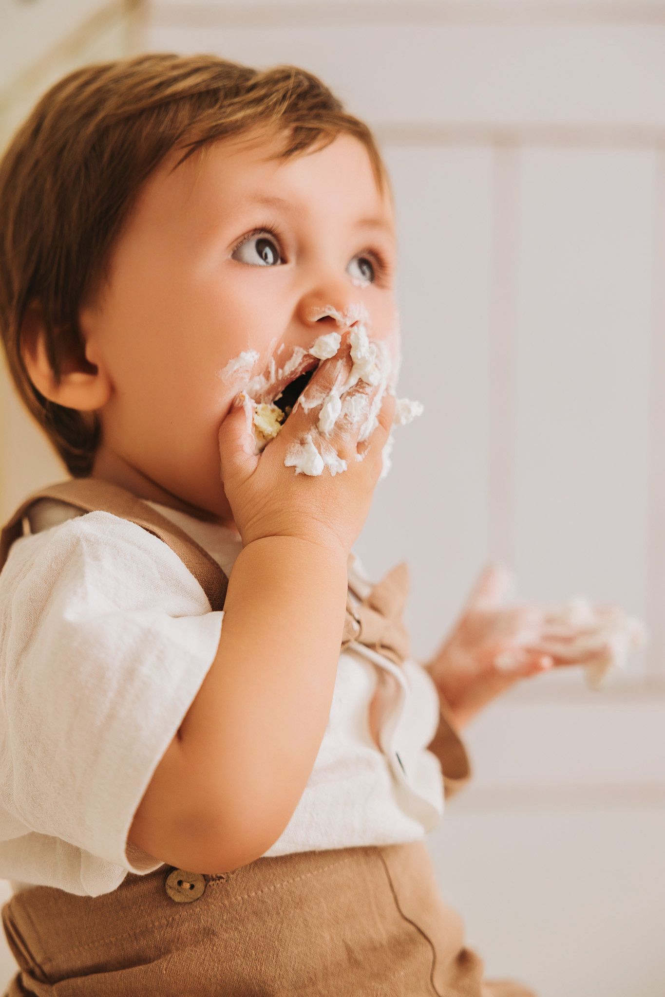 Cute toddler boy with frosting on his face enjoying a cake smash at his first birthday.