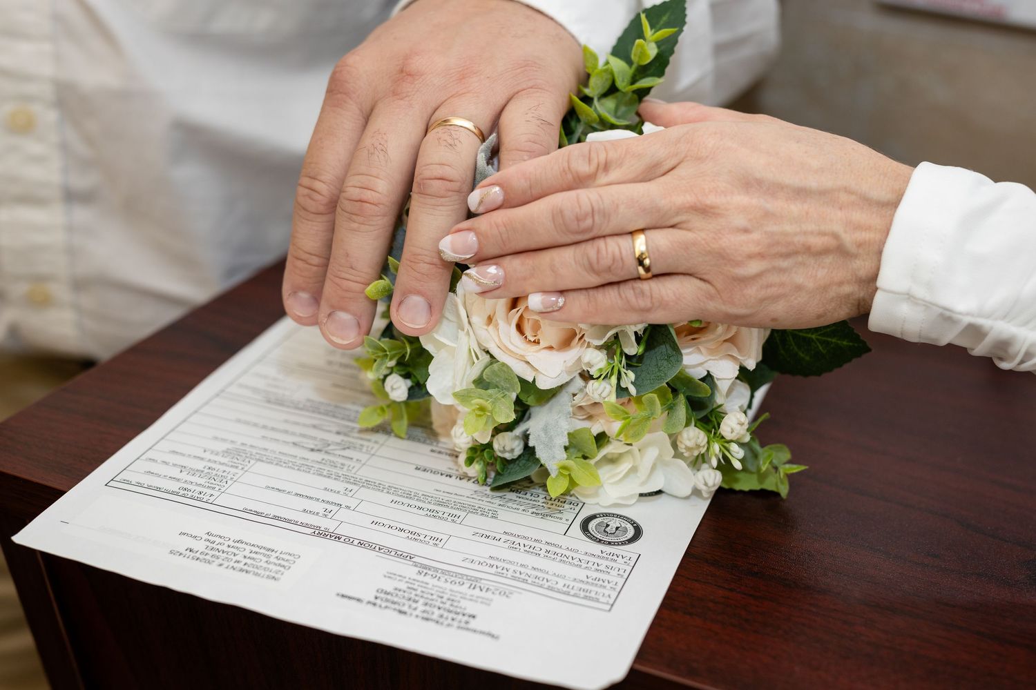 Someone signing documents with a green floral bouquet on a dark wooden table surface.