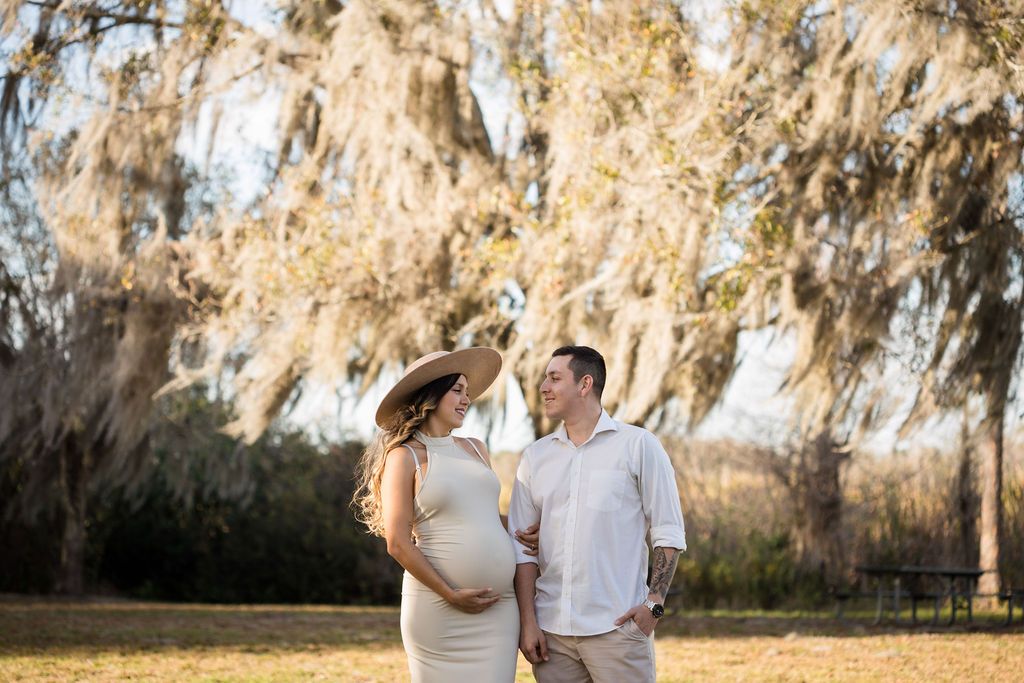 Expecting couple shares tender moment under Spanish moss trees at golden hour.